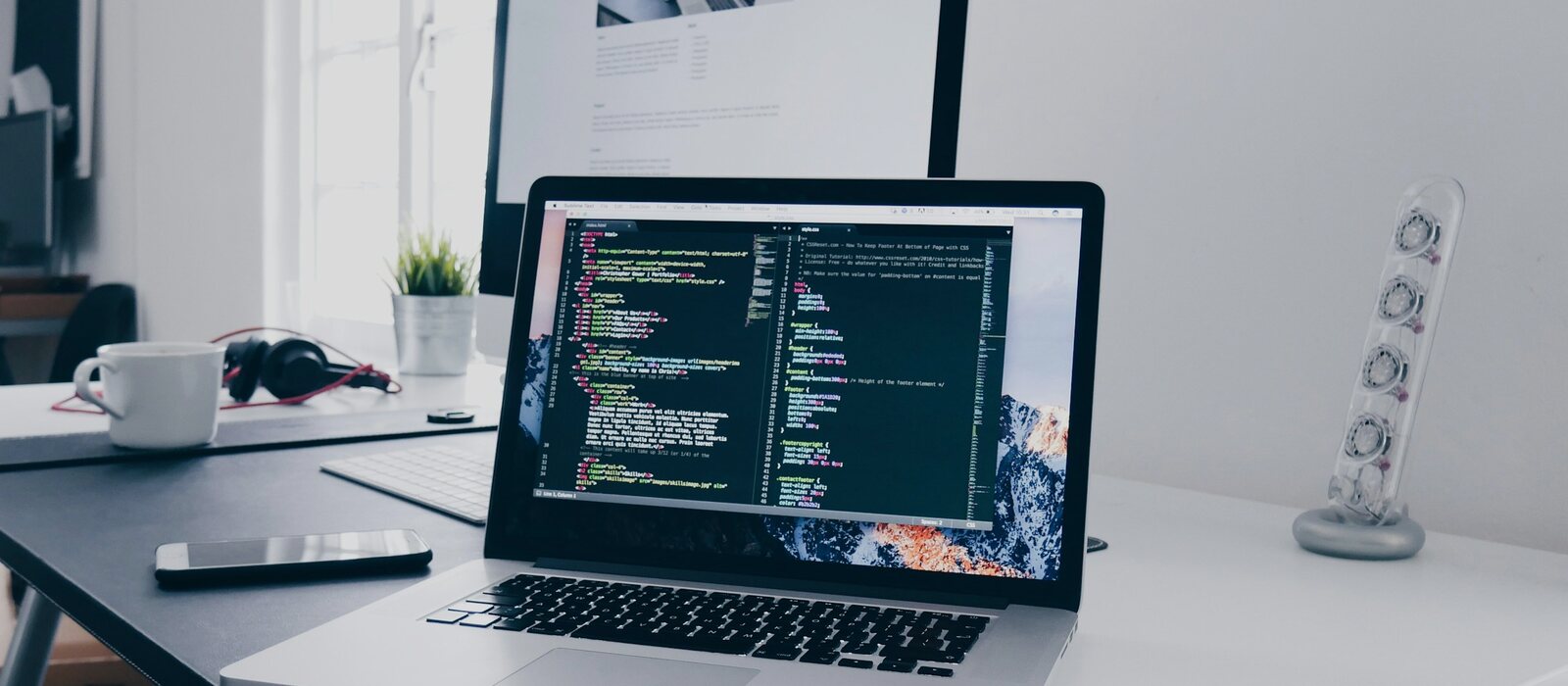 A MacBook with lines of code on its screen on a busy desk